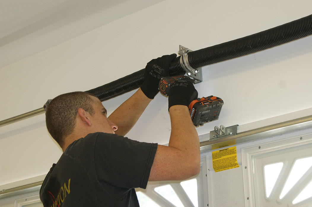 A professional garage technician replacing a garage door torsion spring in a residential garage.